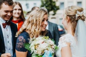 Frau mit gelockten blonden Haaren schaut erwartungsvoll zur Braut