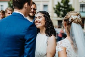 junge Frau mit gelockten dunklen Haaren lächelt gratuliert Brautpaar