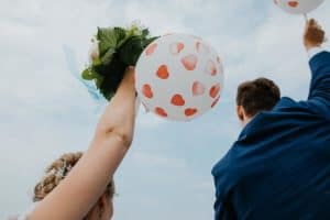 Brautpaar hält Luftballons mit roten Herzen in Luft