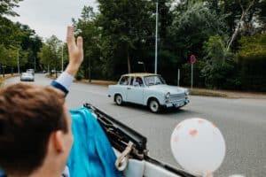 Brautpaar mit Oldtimer Straßenrand altes Auto mit Gästen winken