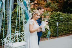 Brautpaar mit Sektgläsern lächelt hält Rede weiße Metallbank blau weiße Bänder