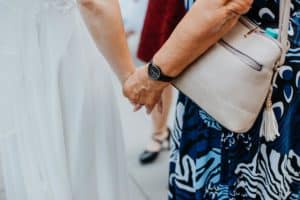Braut in weißem Kleid Hand in Hand mit Oma Armbanduhr beige Handtasche