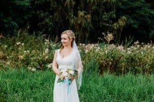 Braut hält Blumenstrauß vor Körper Bäume Wiese