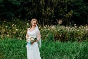 Braut hält Blumenstrauß vor Körper Bäume Wiese