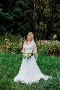 Braut hält Blumenstrauß vor Körper voluminös Kleid Bäume Wiese