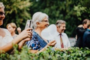 ältere Dame lacht und schaut zum Brautpaar hält herzförmigen weißen Fächer in Hand