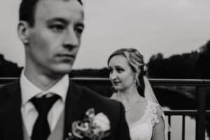 Braut steht hinter Bräutigam schaut zur Seite er ist aber nicht im Fokus