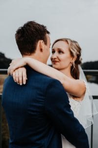 Bräutigam steht mit Rücken zur Kamera Braut legt Arme auf Schultern ab