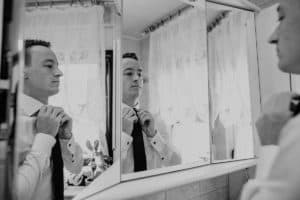 Bräutigam schaut sich im Badezimmerspiegel an richtet Krawatte