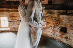 Braut steht hinter Bräutigam und umarmt ihn