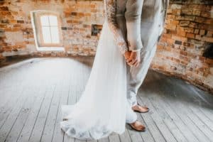 Braut steht hinter Bräutigam und halten Händchen