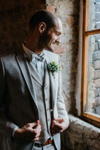 Bräutigam schaut aus Fenster Fliege Anzug Weste Ansteckblume