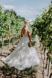 Braut hält Brautstrauß Rückenausschnitt Brautkleid Weinanlage Weinberg