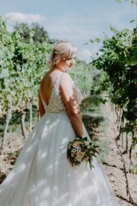 Braut hält Brautstrauß Rückenausschnitt Brautkleid Weinanlage Weinberg