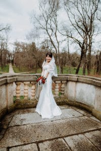 Braut mit Schleier hält Brautstrauß rote Rosen im Park Steinmauer